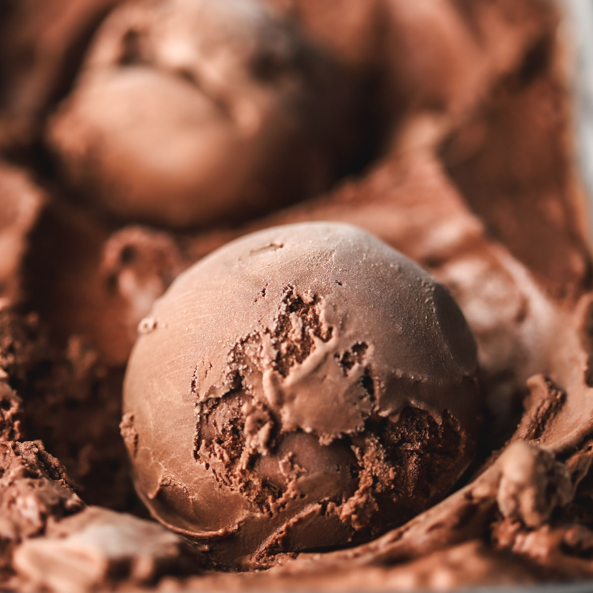A scoop of chocolate ice cream laid on chocolate ice cream.