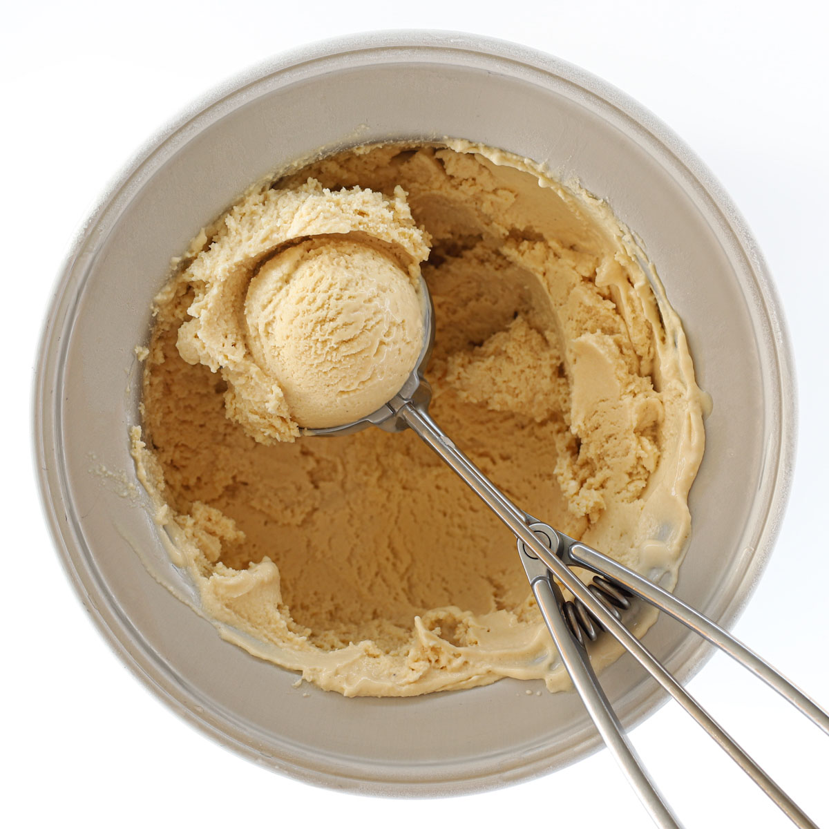 Featured photo for coffee ice cream with egg yolks, shows an ice cream maker bowl filled with coffee ice cream and on it there is scooped coffee ice cream in a scoop.