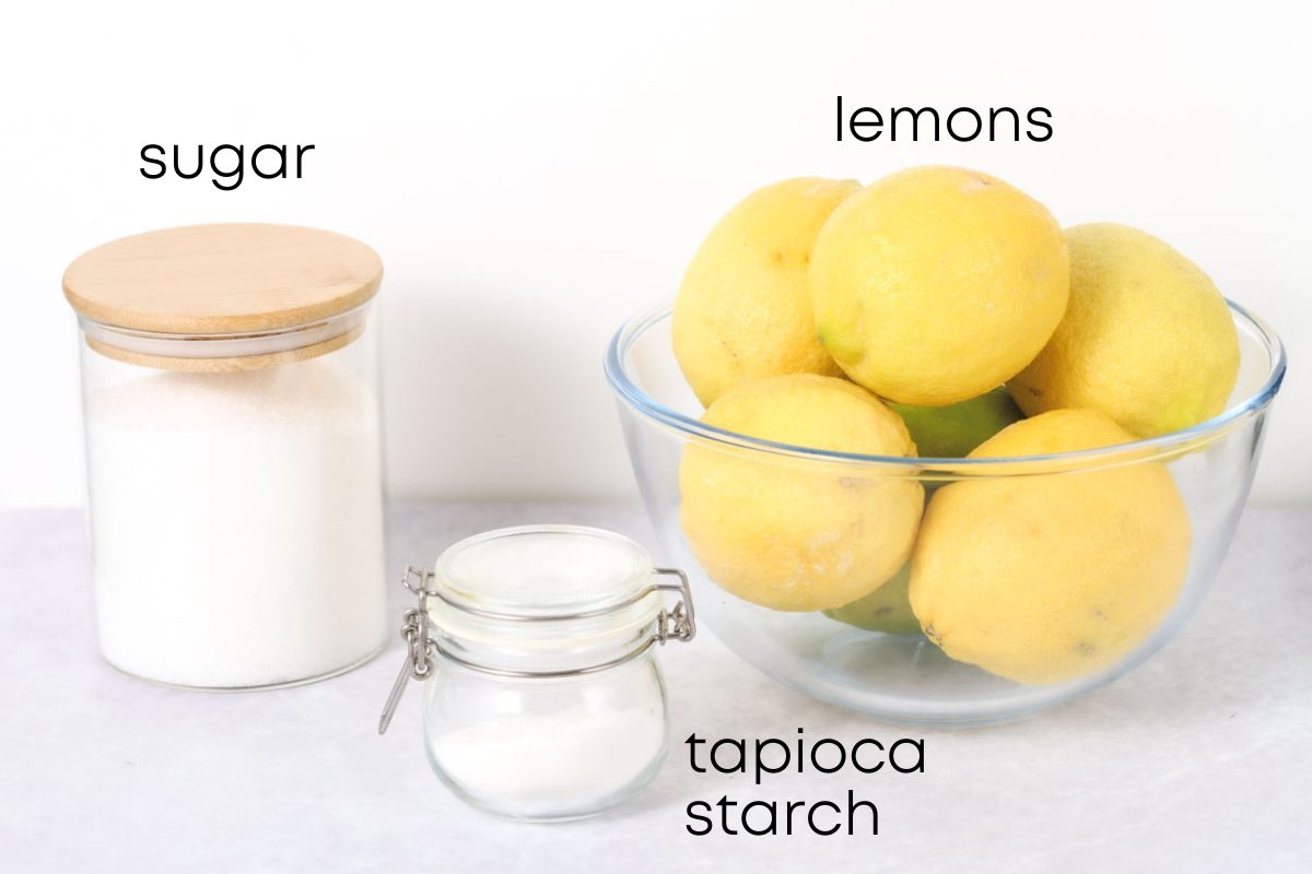 Showng the ingredients of the Lemon sorbet recipe from left to right: a container with sugar, a small container with tapioca starch and a glass bowl full of fresh lemons.